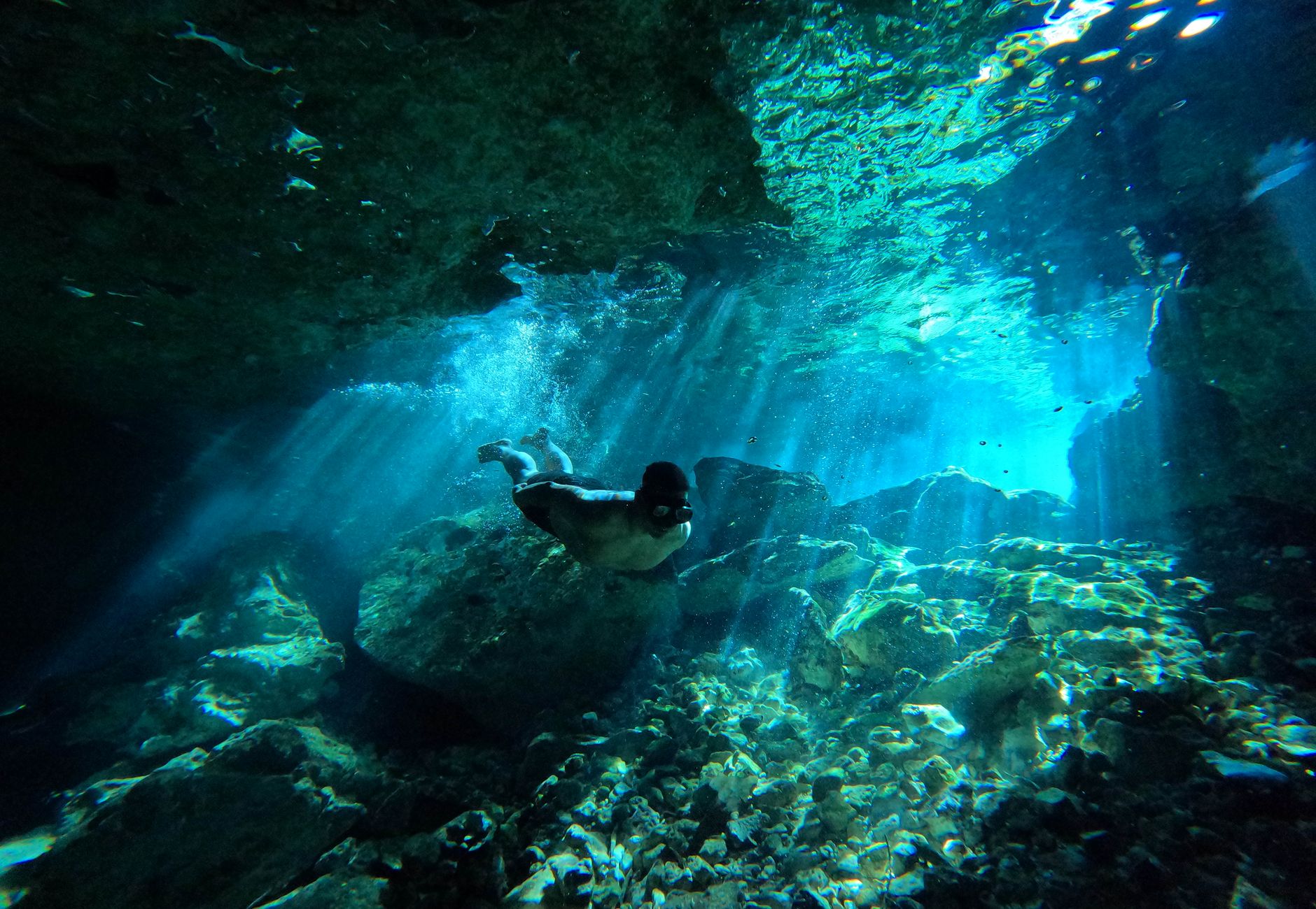 Diver exploring an underwater cave with stunning light beams and vibrant blue hues.