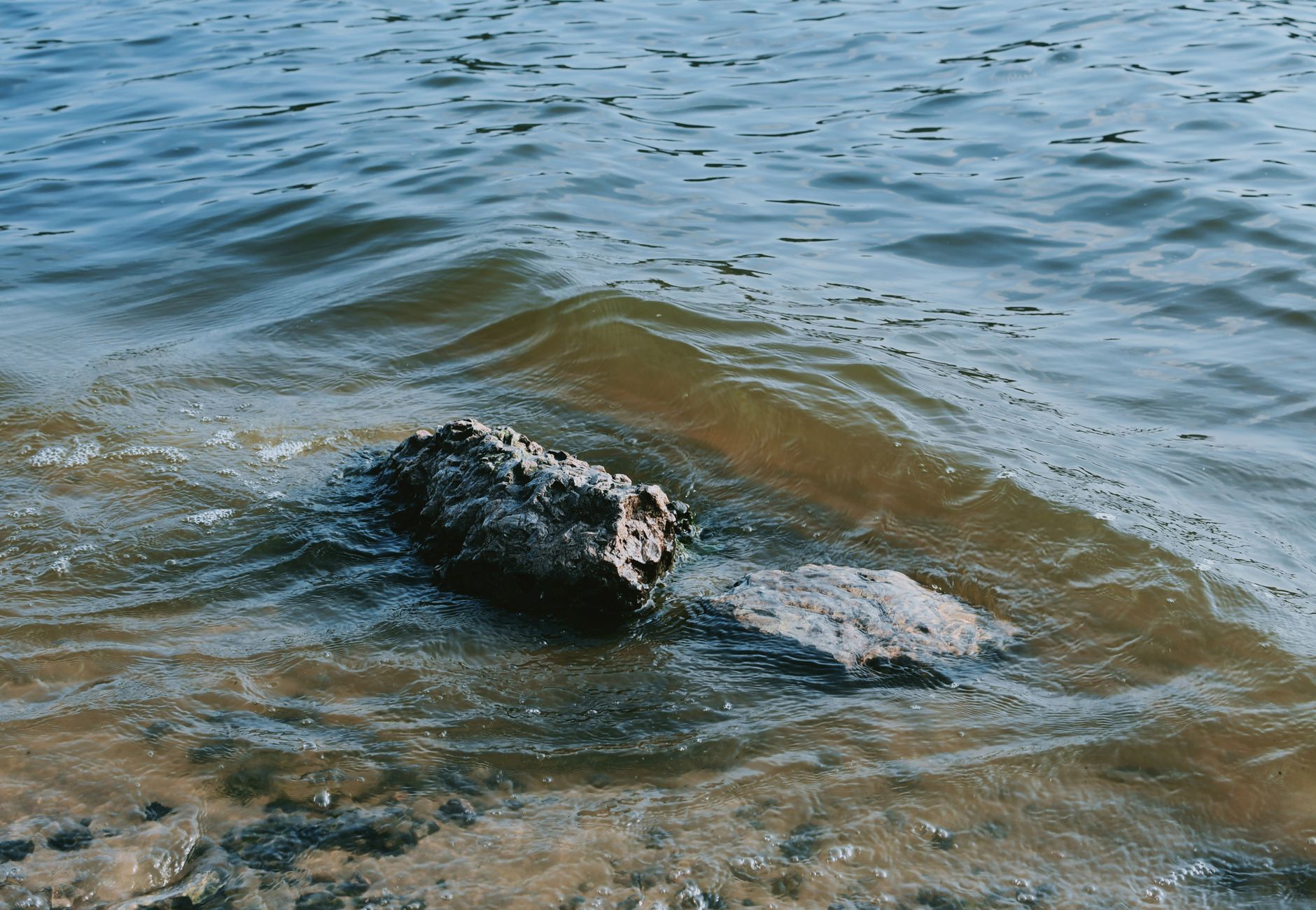 Calm water waves gently lap against a lone rock on the shore, creating a peaceful coastal scene.