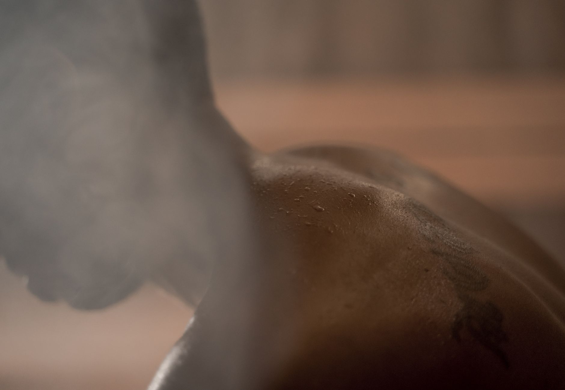 A close-up of a person enjoying a sauna, showcasing a steamy atmosphere and glistening skin.