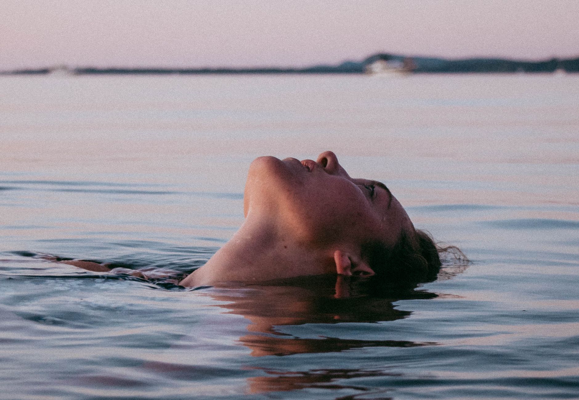 Woman floating on tranquil water during sunset, exuding calmness and relaxation.