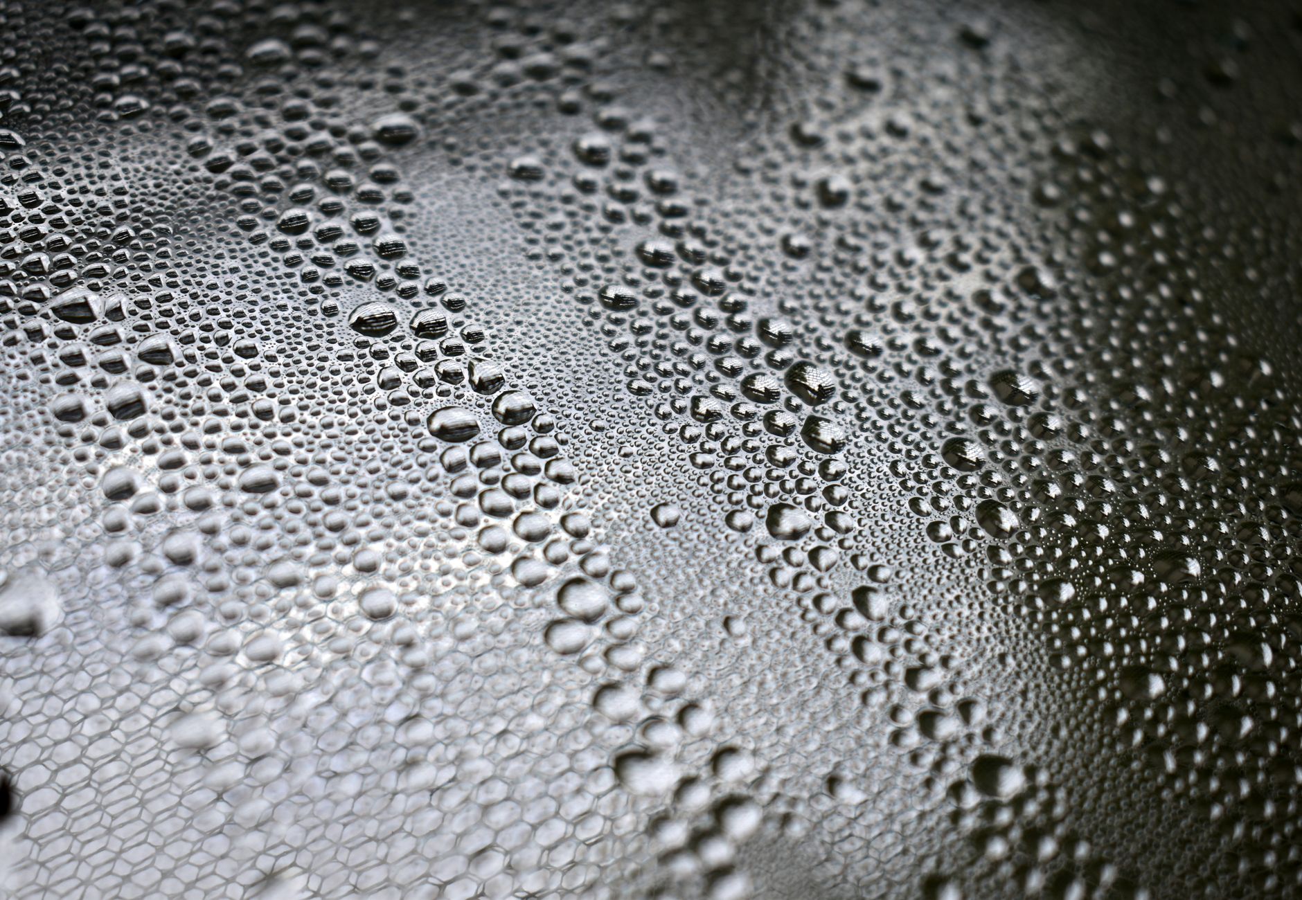 Detailed close-up of water droplets forming patterns on a black surface, showcasing texture and clarity.