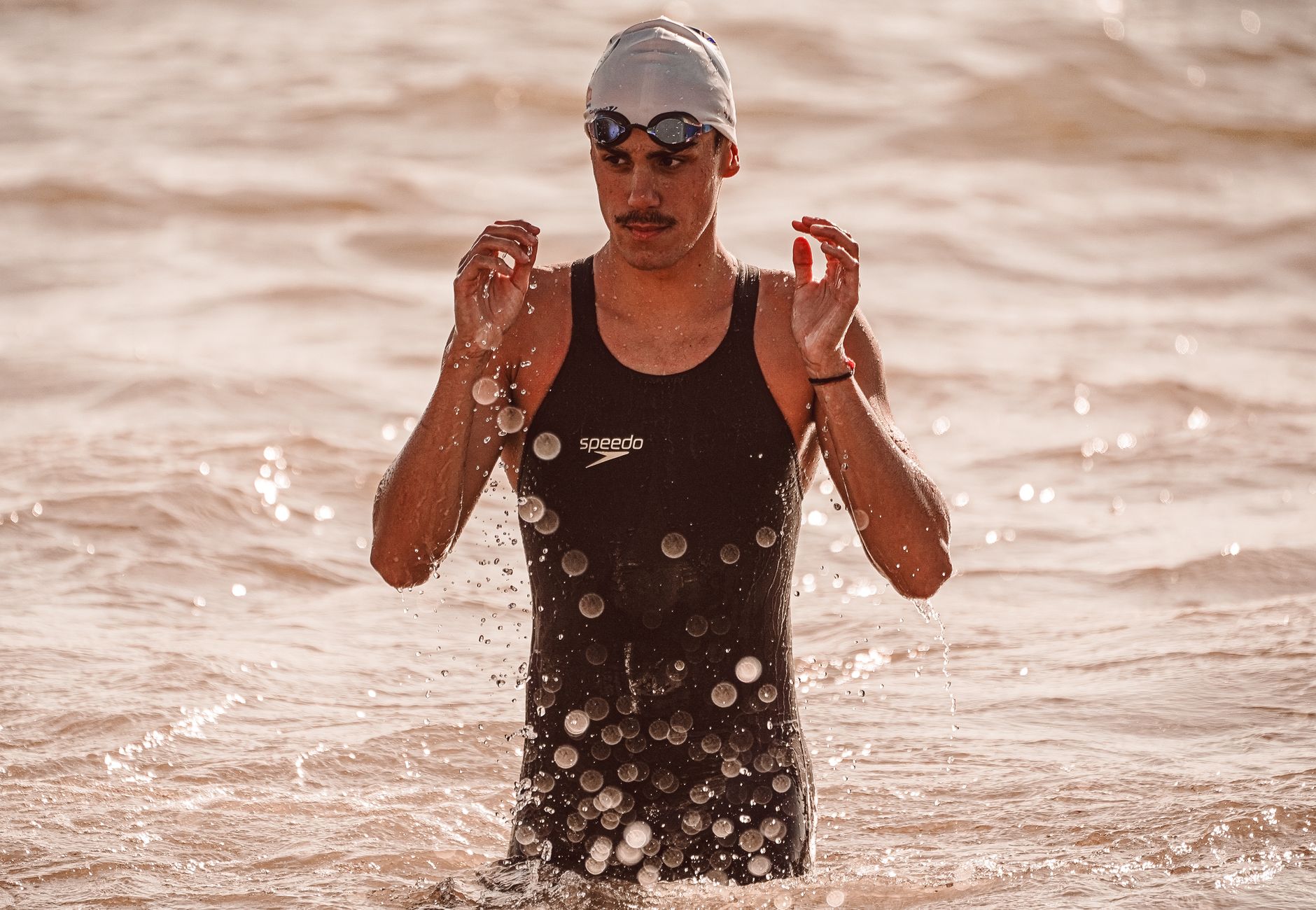A male athlete in swimwear emerges from the sea, showcasing determination and focus.