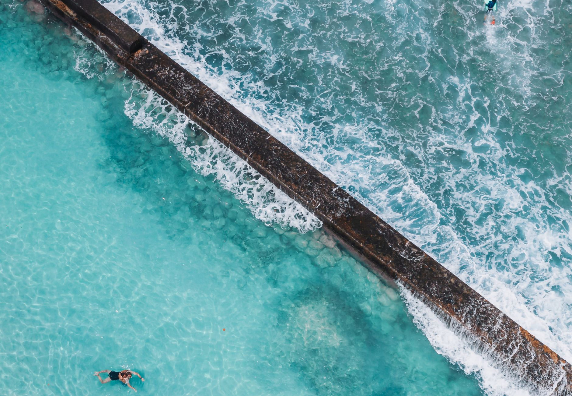 Stunning aerial view of an ocean pool in Hawaii with clear blue waters and ocean waves crashing nearby.