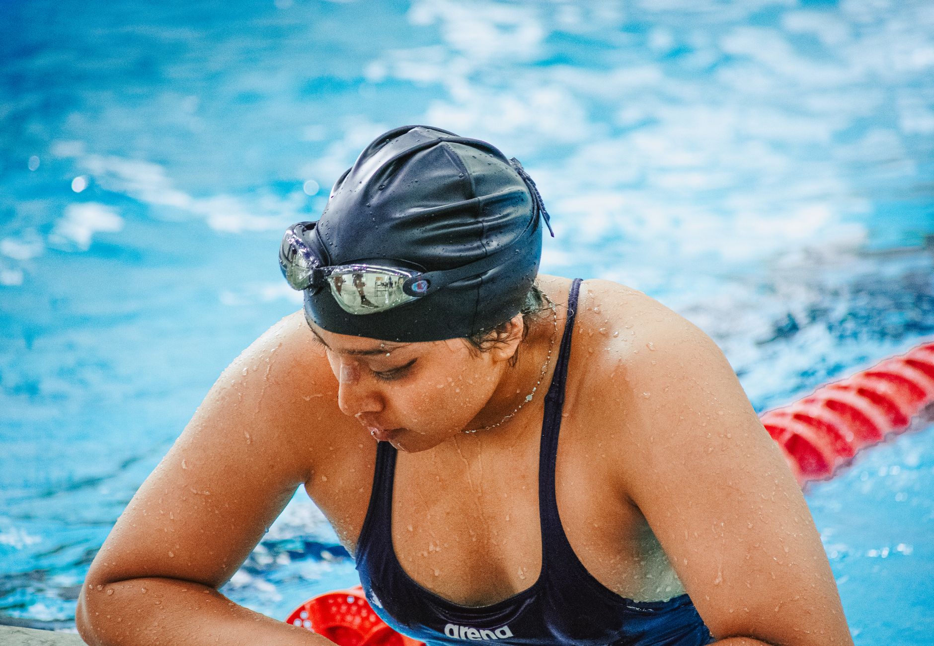 Female swimmer in swim cap and goggles resting poolside, focused and determined.