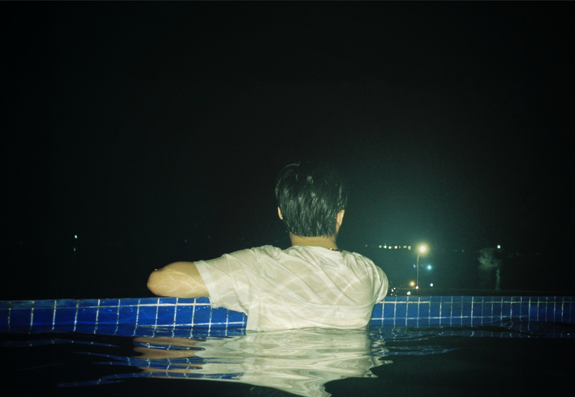 A man enjoying a tranquil moment in a swimming pool at night under the stars.